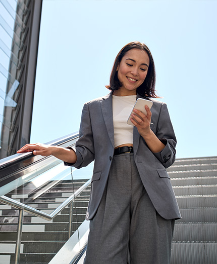 giovane donna sorridente consulta la sua posizione bancaria da smartphone mentre scende le scale mobili