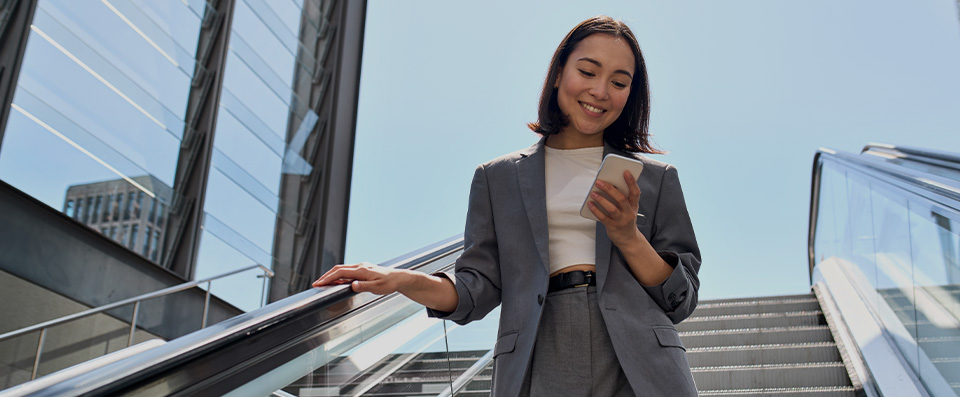 giovane donna sorridente consulta la sua posizione bancaria da smartphone mentre scende le scale mobili