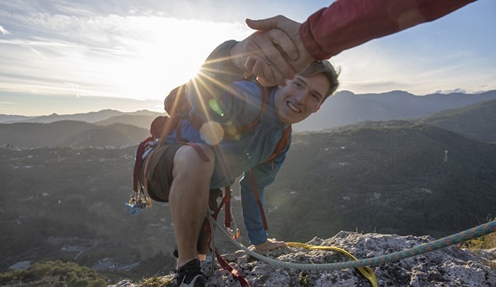 Uomo scala montagna aiutato da altra persona