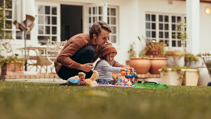 Nel giardino di casa il giovane papà guida con affetto la piccola figlia all'utilizzo di un gioco 