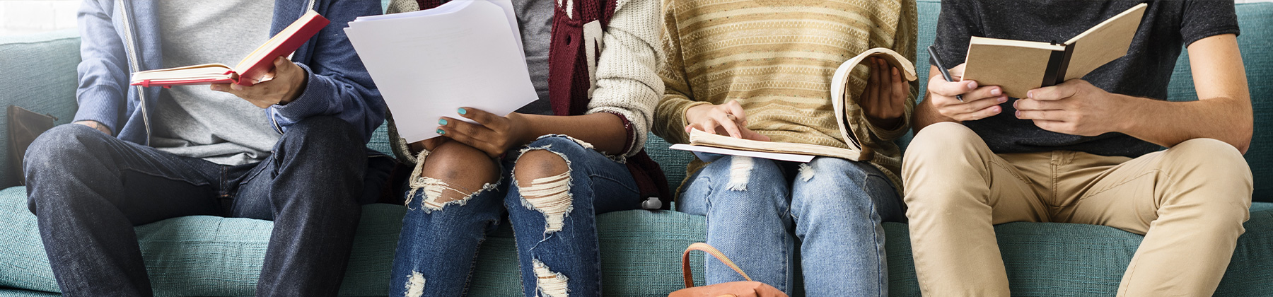 Gruppo di quattro giovani indivdui, di cui non è visibile il volto, sono seduti su divano. Tutti hanno in mano un libro o un quaderno e in atteggiamento amichevole si confrontano sui loro studi.