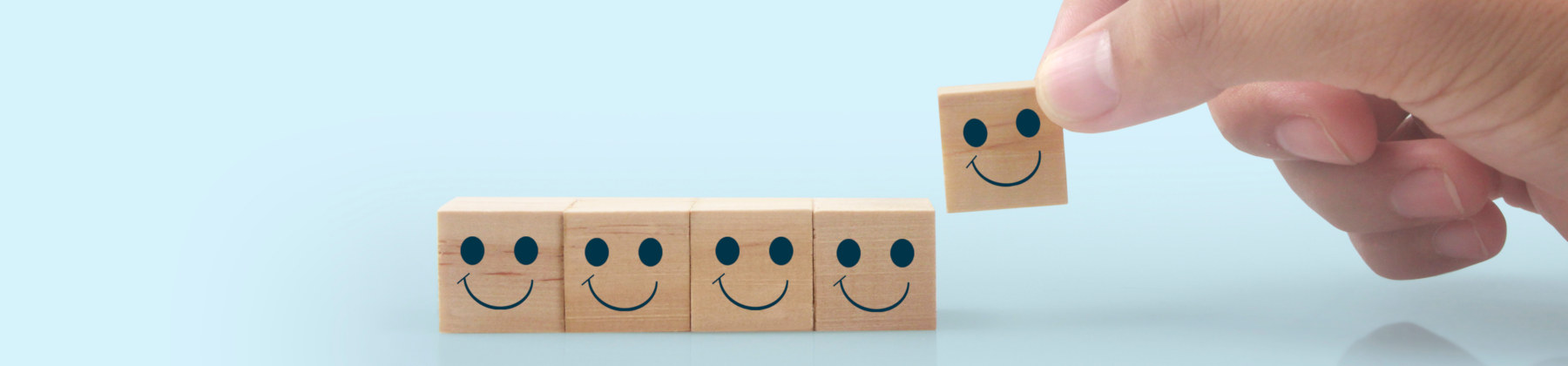 Fotografia di una mano che posiziona su un piano, uno accanto all'altro, dei cubetti di legno con uno smile sulla faccia rivolta verso chi guarda